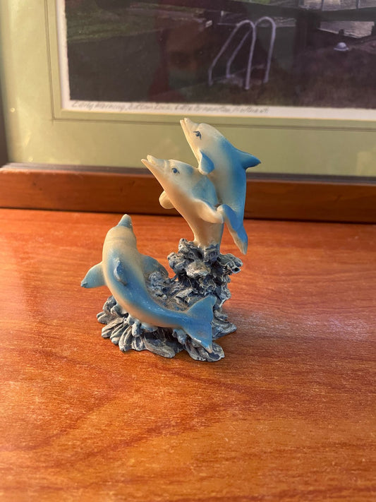 A resin figurine depicting three dolphins on a base resembling a stump and coral reef.