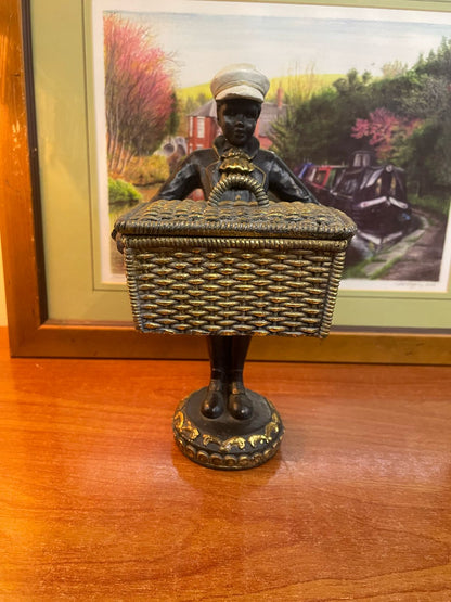 A vintage figurine, possibly colonial-era, featuring a person carrying a basket