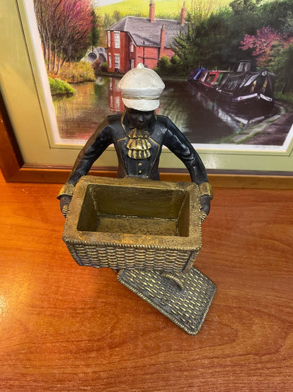 A vintage figurine, possibly colonial-era, featuring a person carrying a basket