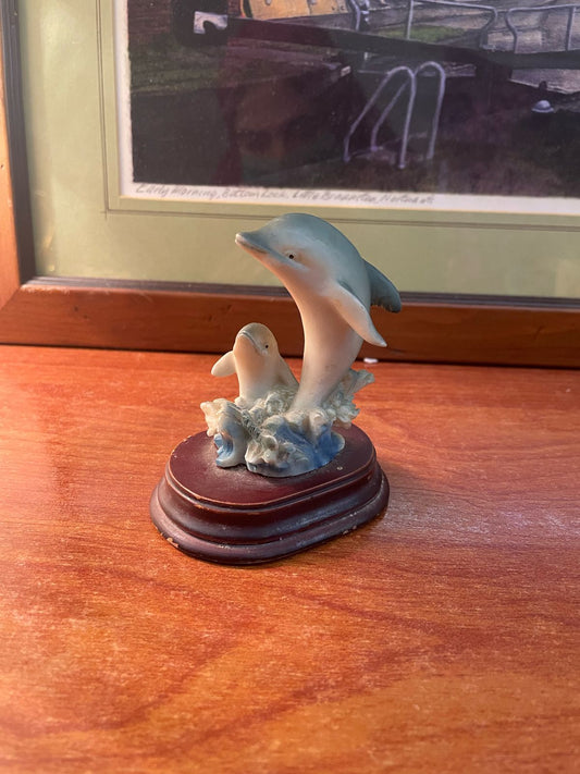 A resin figurine depicting two dolphins on a base resembling a stump and coral reef.